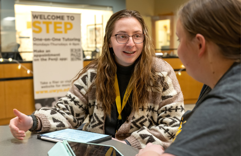 A student mentor at UW’s STEP tutoring center helps another student prepare for public speaking with the STEP sign in the background.