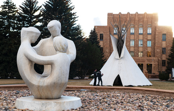 A marble staute of a family holding hands, in the background is a Native American tent.