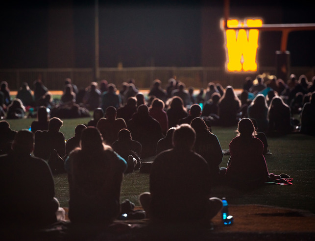 Students sit on blankets to watch a movie on the football field with the University of Wyoming "W" illuminated in the background