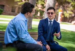 Two UW students sit outside on a bench and discuss pressing student matters