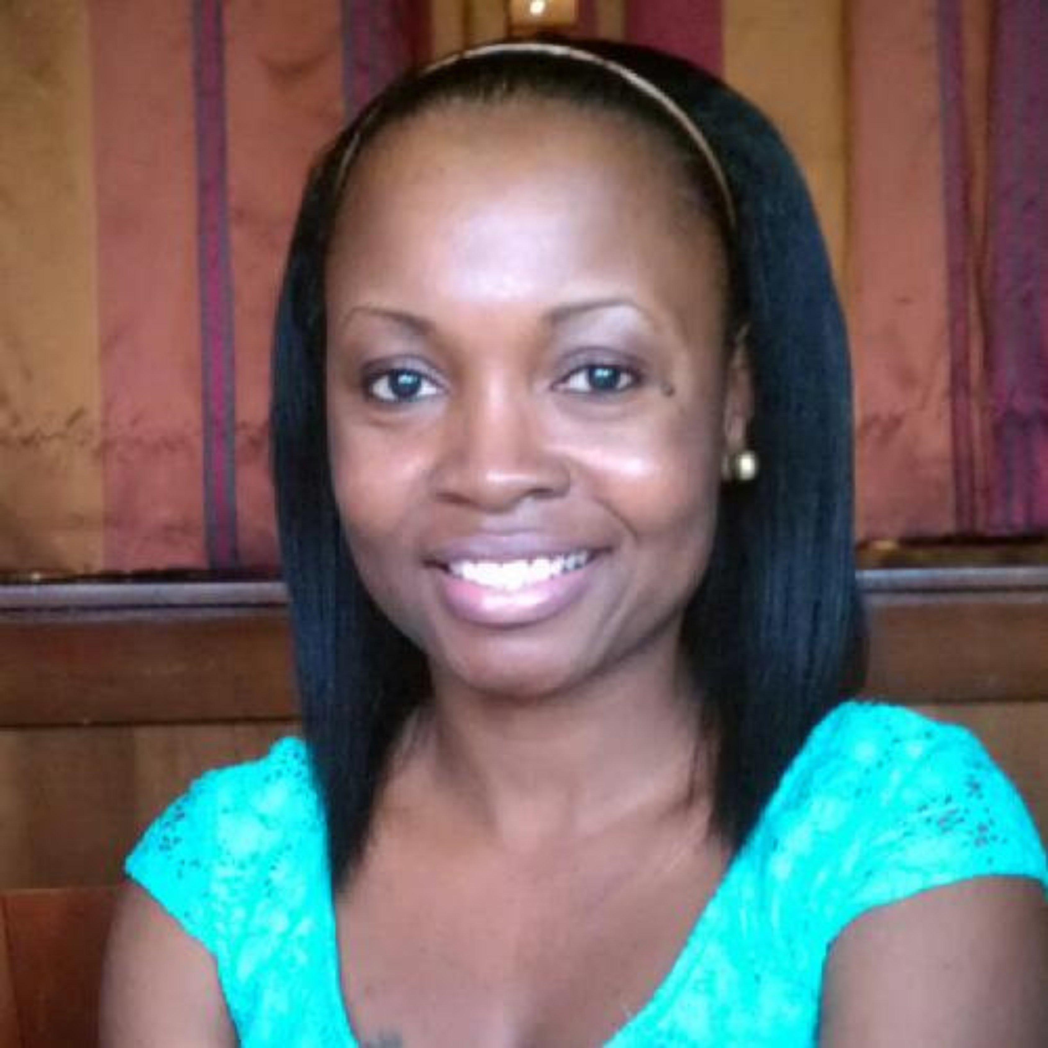 portrait of a woman smiling in front of a wood plank background. dark hair, bright teal shirt.