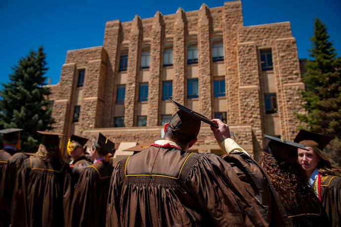 group of UW graduates wearing cap and gowns facing UW building