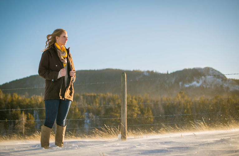 A student standing in snow next to a fence looking off to the side