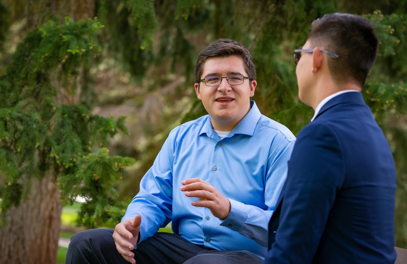 Two UW students sit on a bench on the University of Wyoming campus and have a conversation.