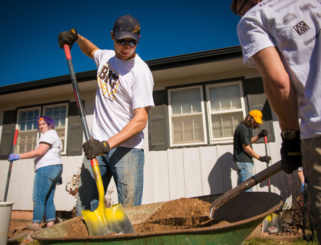 Two students volunteering with shovels and wheelbarrow