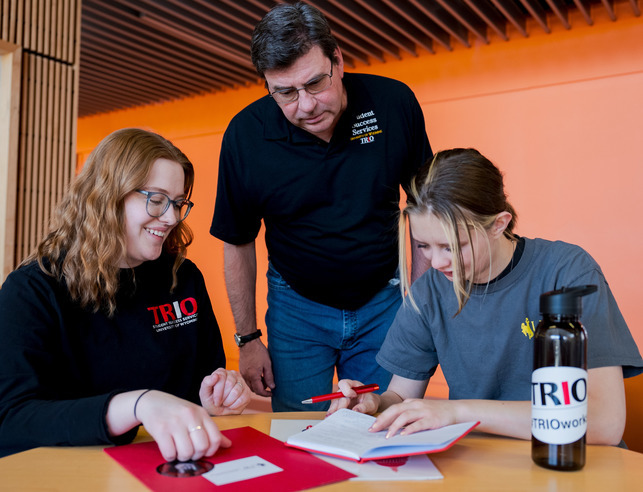 Two students and faculty working at a table