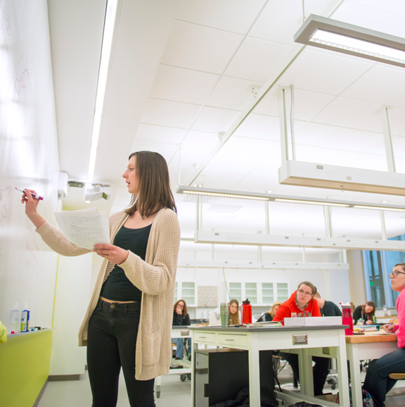 an instructor writing on a whiteboard while students look on attentively
