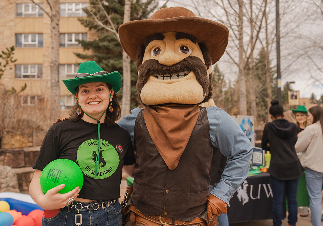 A Green Dot facilitator in a green cowboy hat poses with UW mascot Pistol Pete