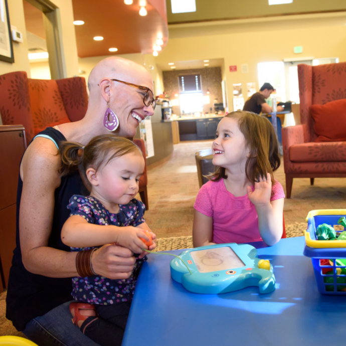 adult woman at a table with two young children and toy food.