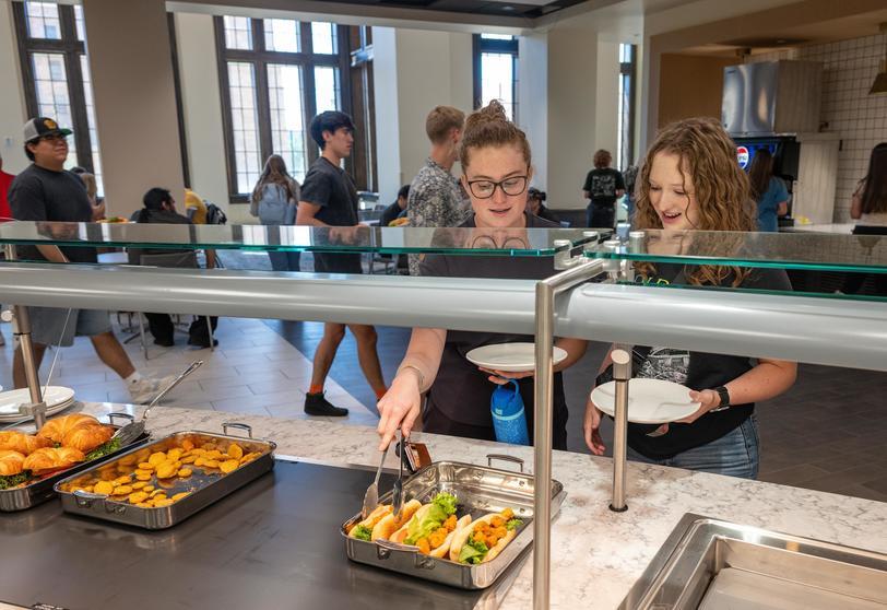 Two students selecting food from a dining hall station