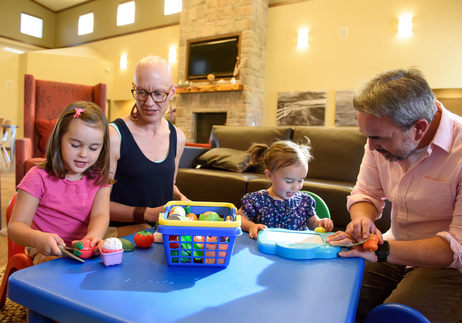 A mother and father with two young children playing with toys at a table