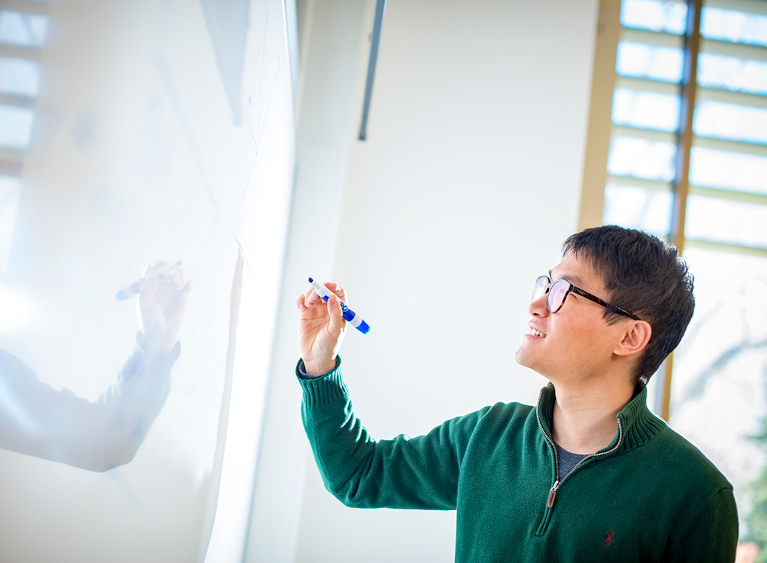 student writing on a white board in class