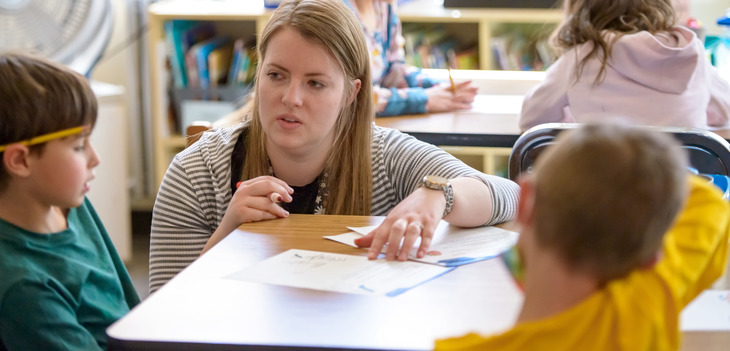 Education student helps two young students with an assignment