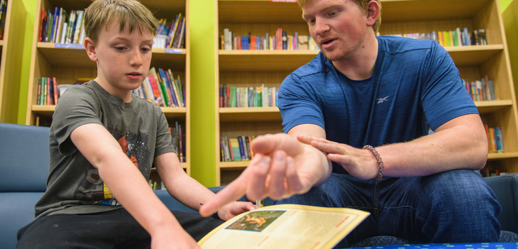 Education student and a youth reading a book in library