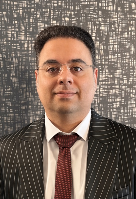 Dr. Amin Davoodi in a white shirt and black suit jacket, with a red check tie