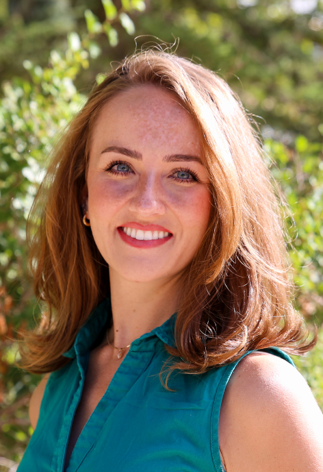 Regin Dean in a teal blouse in front of a leafy landscape