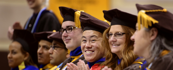 doctoral students in full regailia smile during a commencement ceremony