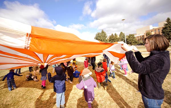 A group of kids and student teaching student us a parachute in Prexy's Pasture