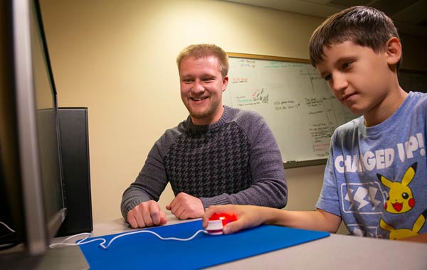 A student teacher works with a child at a computer.