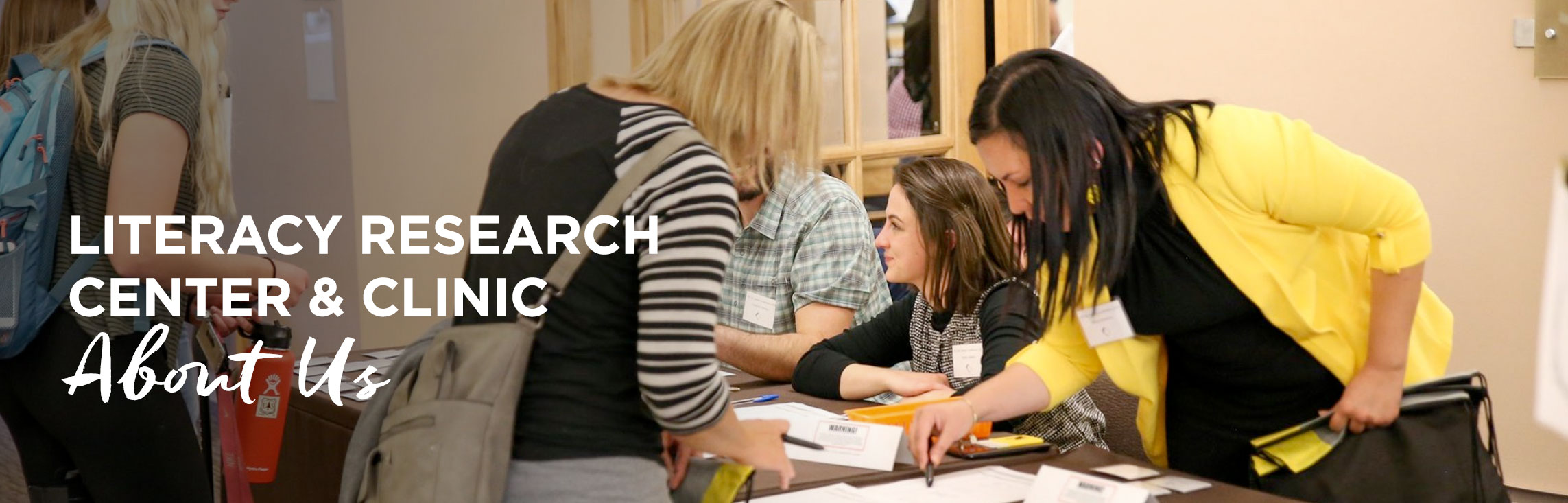 Teachers looking at papers at a conference with wording: Literacy Research Center & Clinic About Us