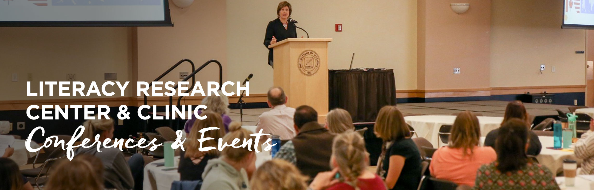 Teachers watching speaker at conference with wording: Literacy Research Center & Clinic Conferences & Events