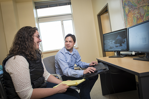 a graduate student receives advising from a faculty member while sitting at a desk in an office