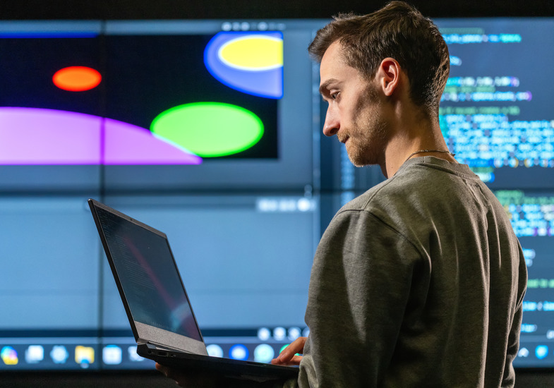 A computer science student examines code on their laptop with code in the background on a projector screen