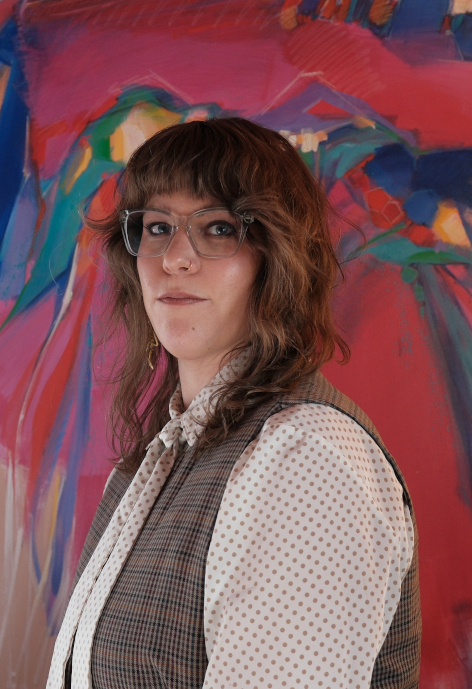 Woman in a vest standing in front of a painted wall.