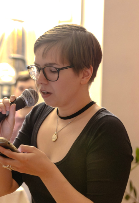Young woman with glasses speaks into a microphone.