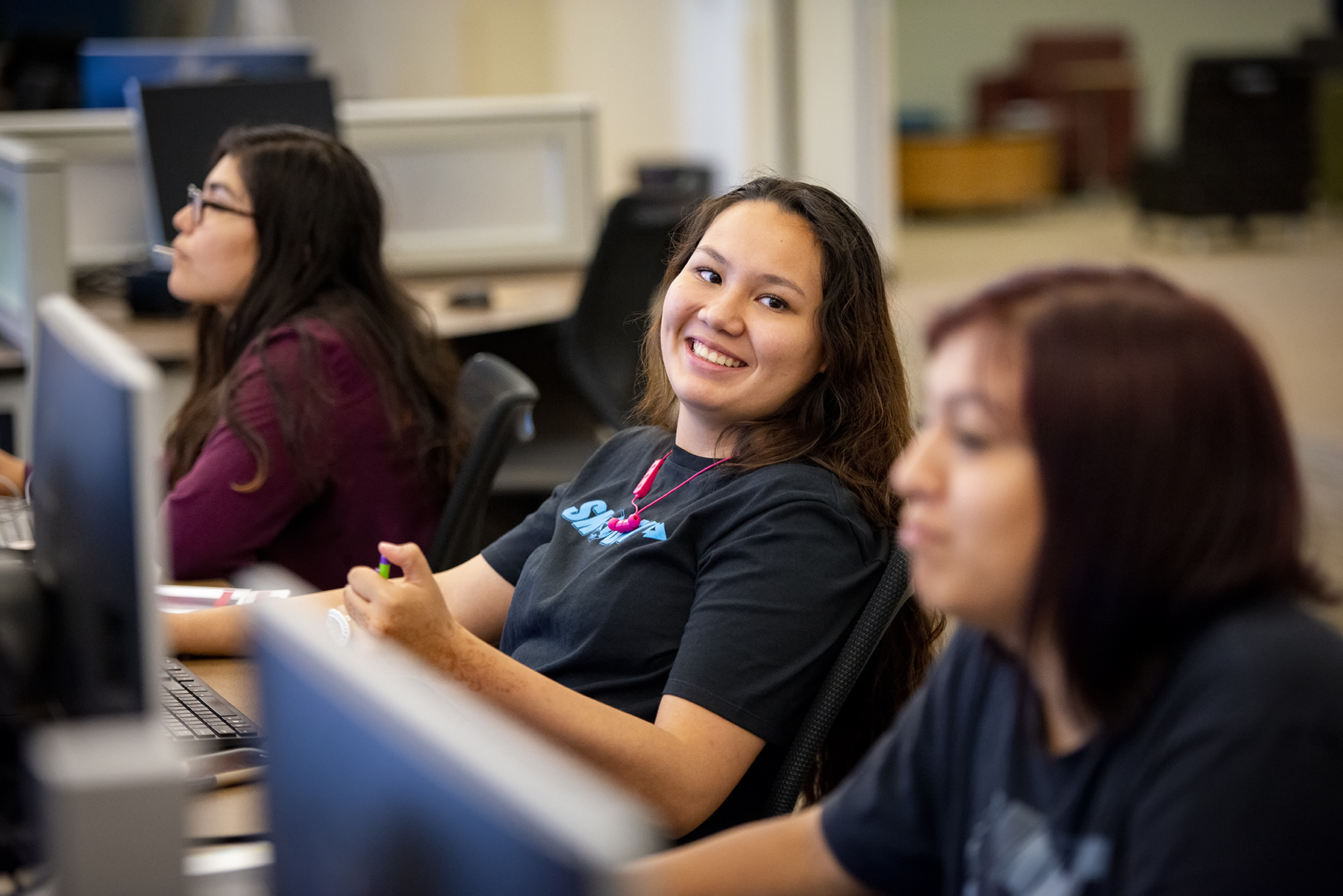 three students smile while working on computers