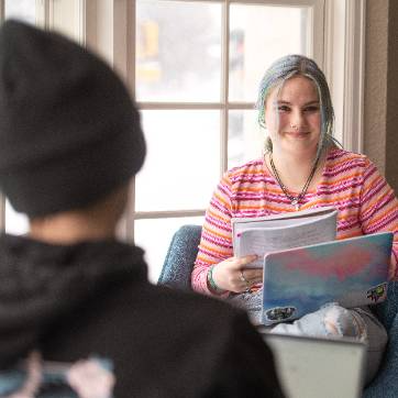 a student is interacting with another while holding a notebook