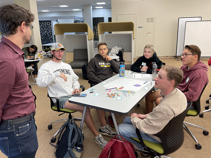 instructor interacts with a table of students in a class discussion