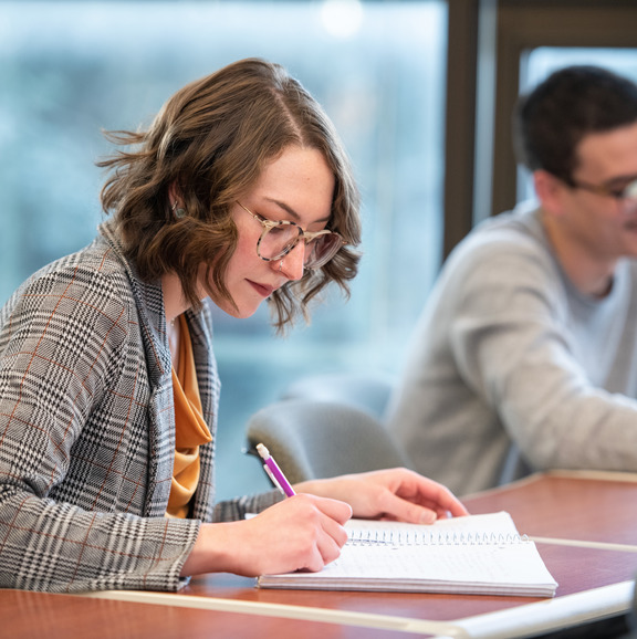 Photo of a woman taking notes which when clicked directs to the Our Team page