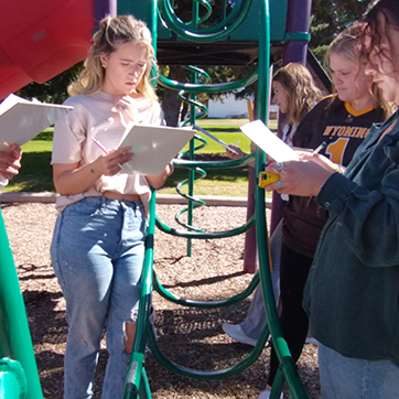 four human development and family studies students in a children's park studying the jungle gym