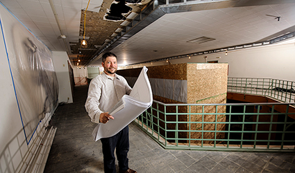 student on a construction site holds floor plans