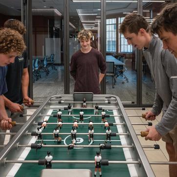 Four University of Wyoming students play foosball in North Hall while one watches.