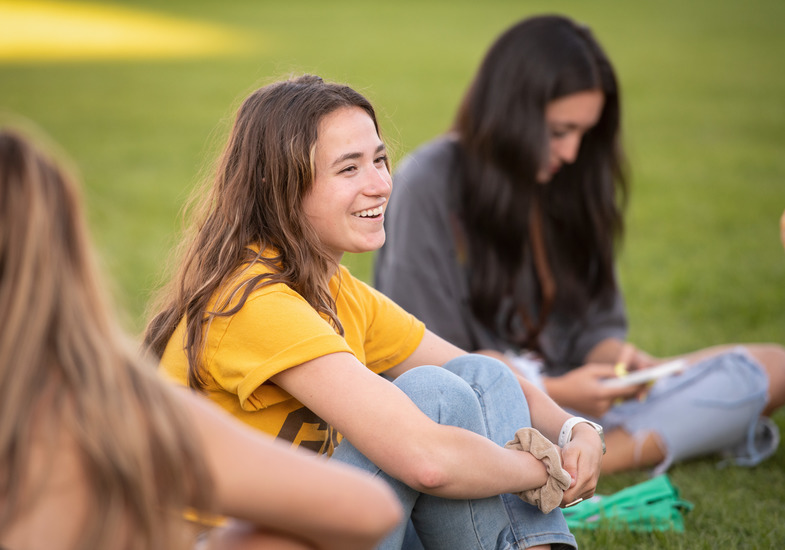 A UW student sits with a group on Prexy’s Pasture and smiles at their friends.