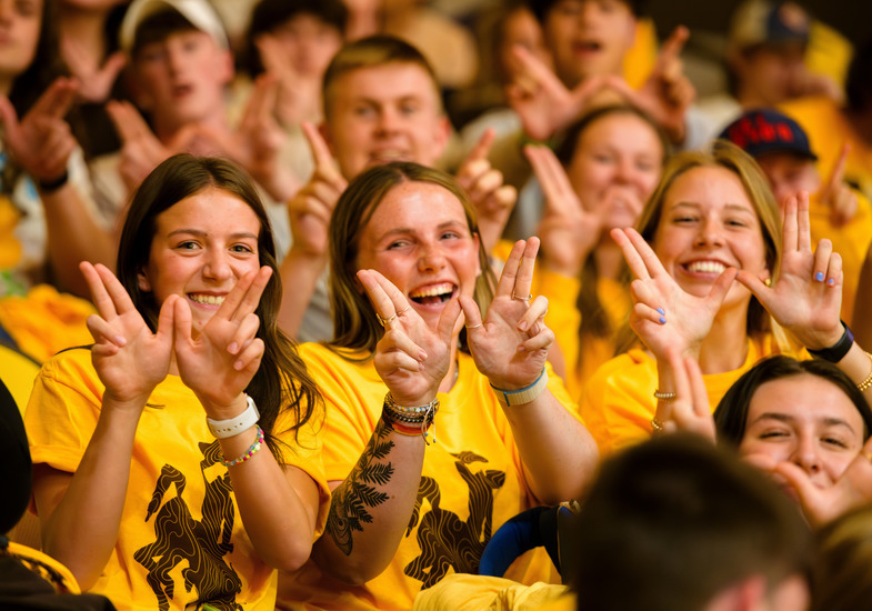 Three UW students sit together at a University of Wyoming event and smile as they make “W”s with their hands.
