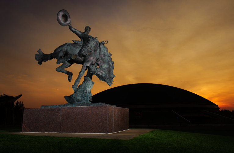 sunset behind bucking horse and rider statue and arena auditorium