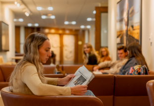 student sitting in a chair reading a newspaper