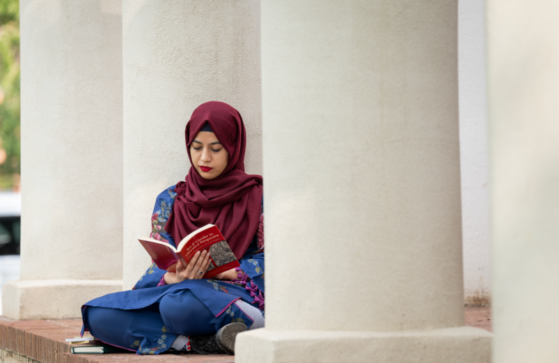 student reading against a building pillar
