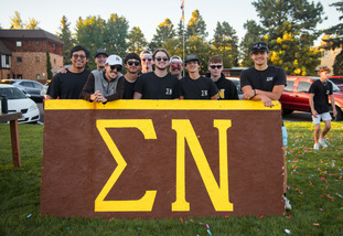 A group of fraternity brothers stand behind a sign for their fraternity at one of UW’s fraternity events
