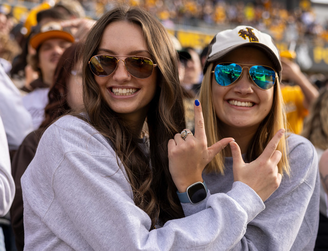 Two students smile and create a "W" with their hands at a football game
