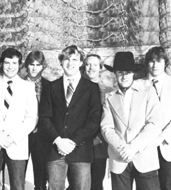 Men posing for a group photo, all in jeans, jacket and tie. One is in a cowboy hat.