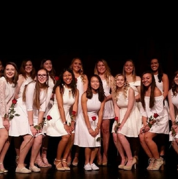 A group of girls, all in white dresses with red roses in their hands, posing after initiation