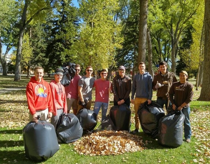 10 members with garbage bags full of leaves and a pile of leaves in front after helping at a service day project 
