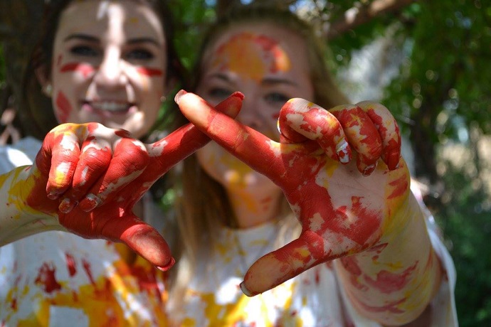 two girls making the chi omega hand sign with red and yellow paint on their hands