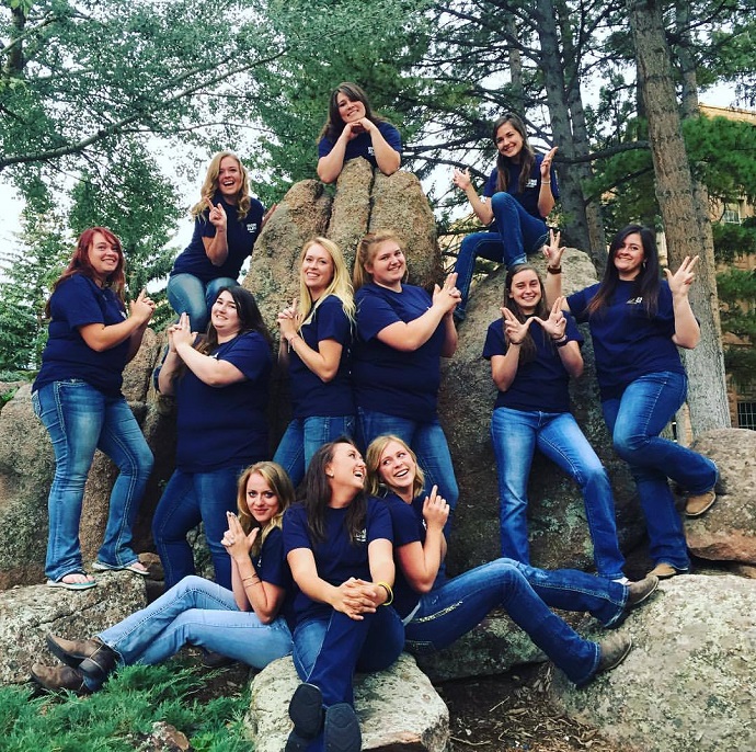 Group photo of members in matching t shirts and jeans posing on a rock
