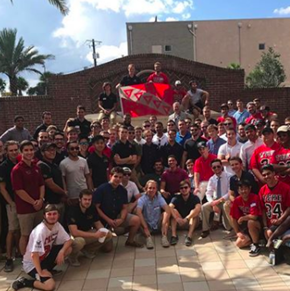 Members of the fraternity holding the TKE flag, most members dressed in red, one of the fraternity's colors.