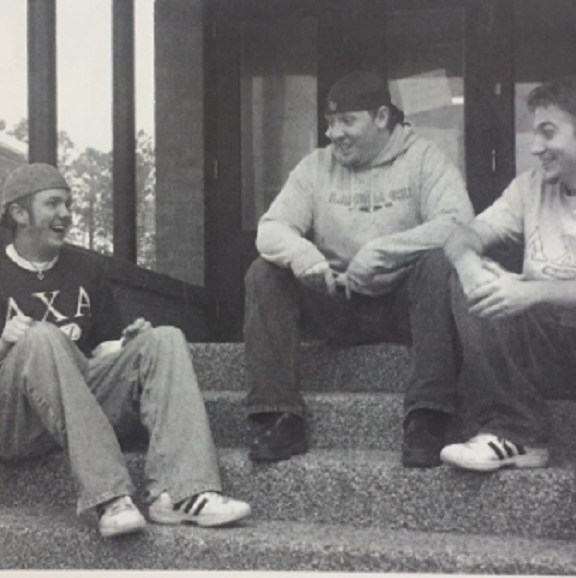 Three boys with fraternity letters on their clothes, sitting on steps